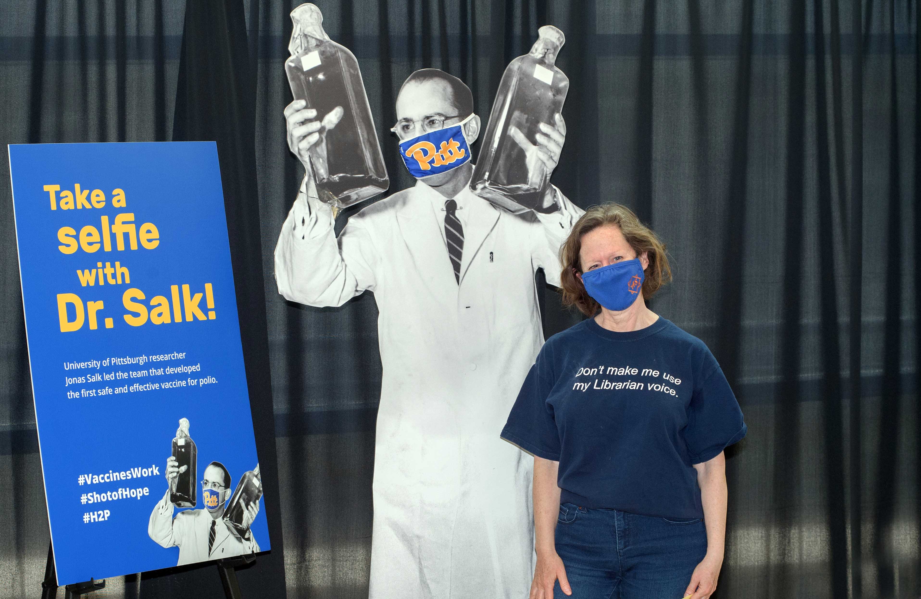 Woman in mask standing next to cutout of Dr. Salk